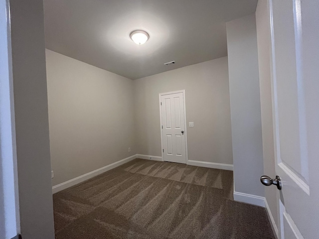 spare room featuring dark carpet, visible vents, and baseboards