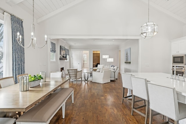 dining room featuring a large fireplace, a chandelier, dark wood-type flooring, high vaulted ceiling, and beam ceiling