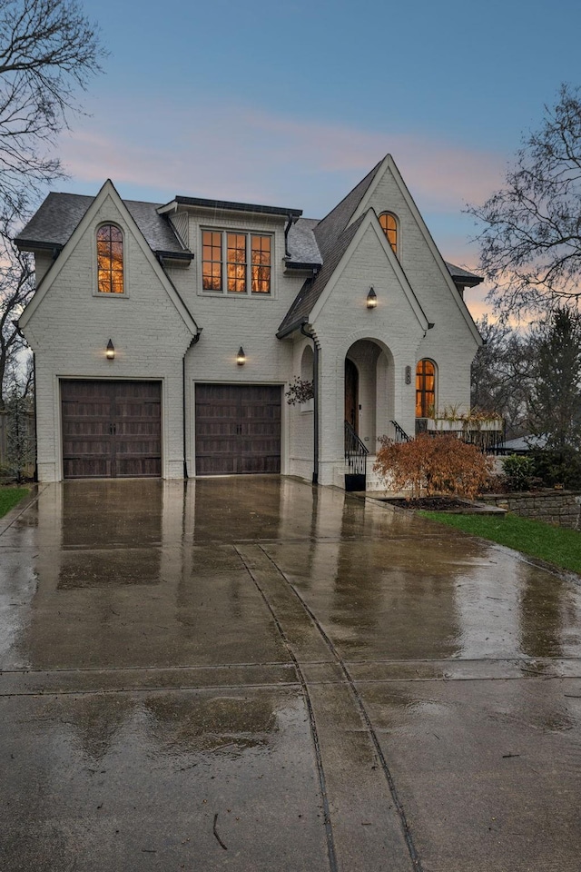 french country style house featuring a garage, driveway, and brick siding