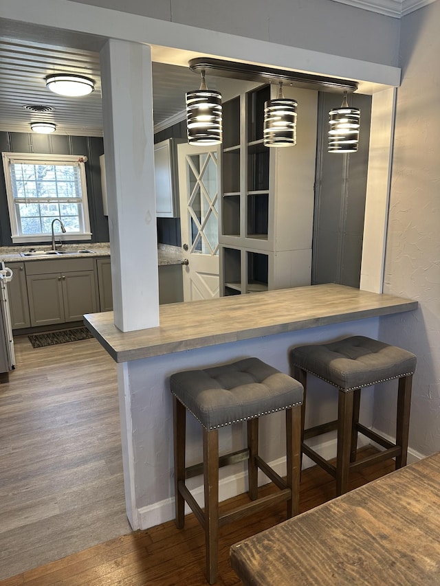 kitchen featuring a breakfast bar area, gray cabinets, a sink, and pendant lighting