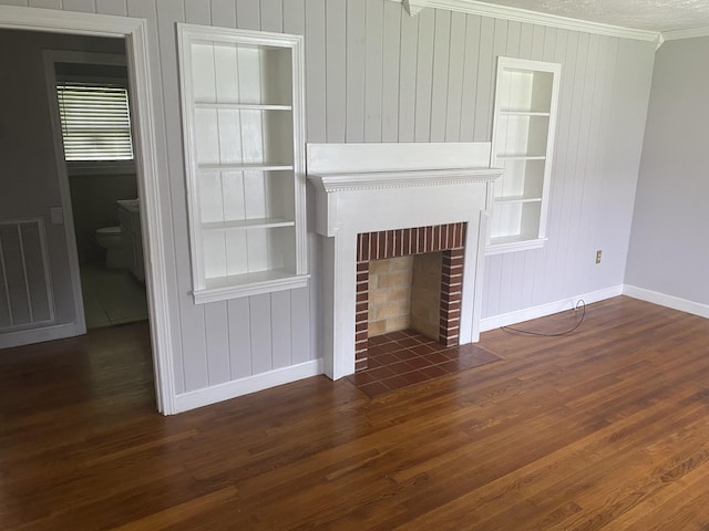 unfurnished living room featuring built in shelves, visible vents, a brick fireplace, dark wood-style floors, and crown molding