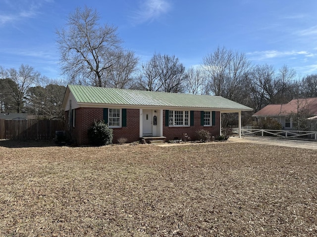 ranch-style home featuring an attached carport, metal roof, brick siding, and fence