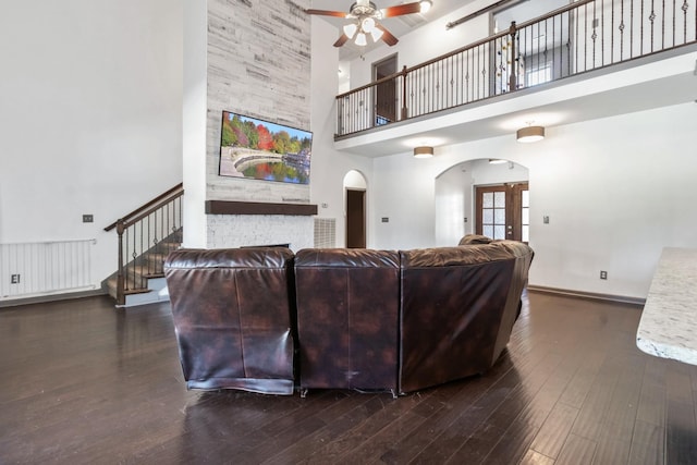 living area with arched walkways, a towering ceiling, dark wood-type flooring, ceiling fan, and baseboards