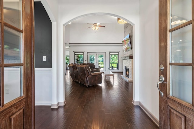 entrance foyer with ceiling fan, a stone fireplace, dark wood-type flooring, a towering ceiling, and baseboards