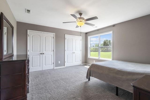 bedroom featuring carpet, two closets, visible vents, a ceiling fan, and baseboards