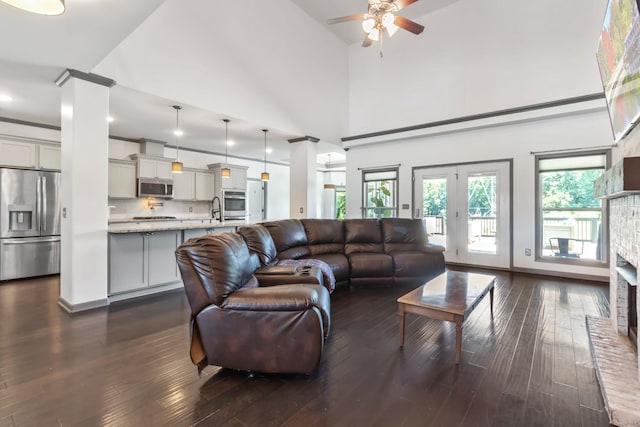 living room with ceiling fan, a brick fireplace, dark wood finished floors, and decorative columns