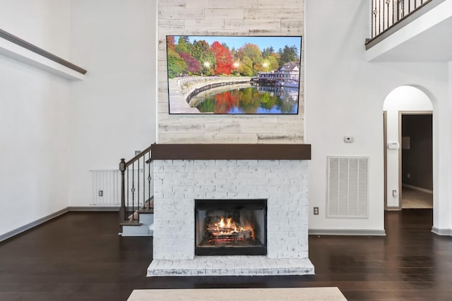 unfurnished living room featuring baseboards, visible vents, dark wood-style flooring, stairs, and a brick fireplace