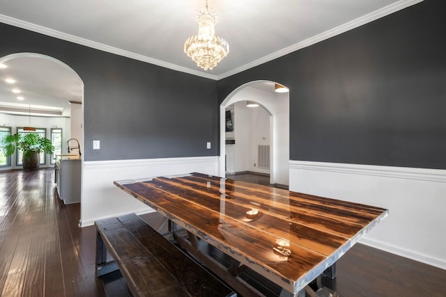 dining space with ornamental molding, arched walkways, dark wood-style flooring, and an inviting chandelier