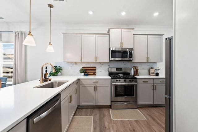 kitchen featuring gray cabinetry, stainless steel appliances, a sink, hanging light fixtures, and light countertops