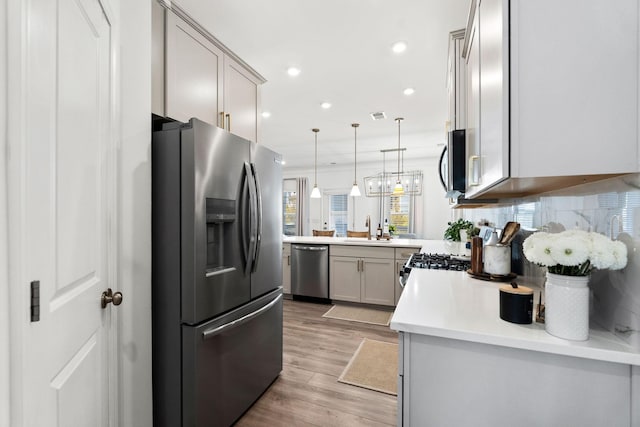 kitchen with light countertops, gray cabinetry, appliances with stainless steel finishes, a sink, and a peninsula