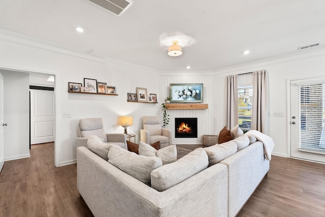 living room with a large fireplace, wood finished floors, visible vents, and crown molding