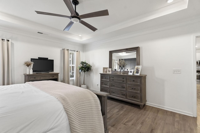 bedroom with crown molding, a tray ceiling, dark wood finished floors, and baseboards