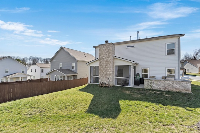 back of property with a yard, a chimney, a sunroom, fence, and a residential view