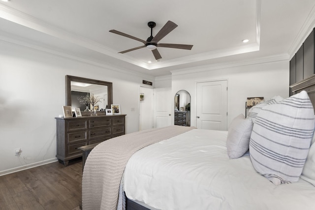 bedroom with dark wood-style floors, a tray ceiling, ornamental molding, and baseboards