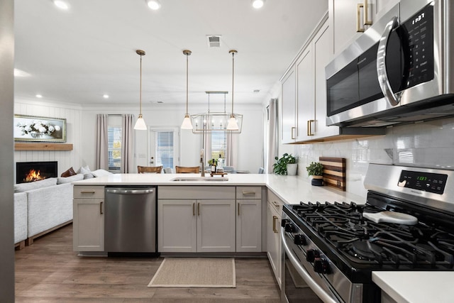 kitchen featuring stainless steel appliances, a peninsula, a sink, open floor plan, and light countertops