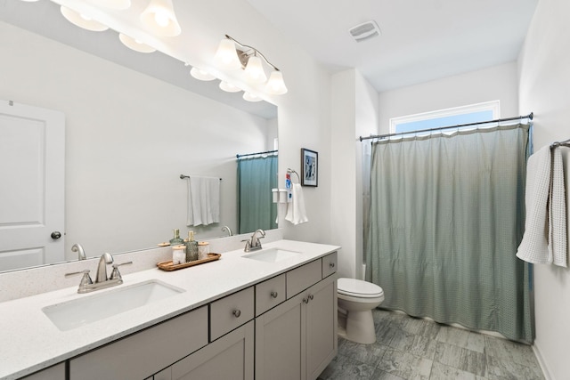 bathroom featuring visible vents, a sink, toilet, and double vanity