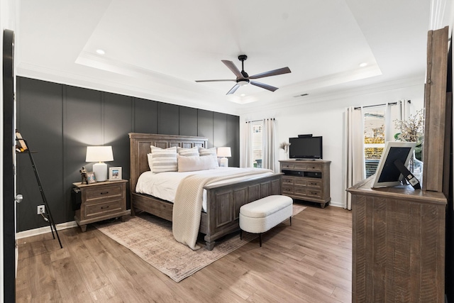 bedroom with crown molding, a tray ceiling, a decorative wall, and light wood-style floors