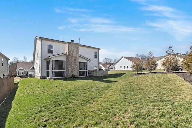 back of property with a sunroom, a residential view, fence, and a yard