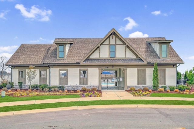 view of front of house with stone siding, a shingled roof, and fence