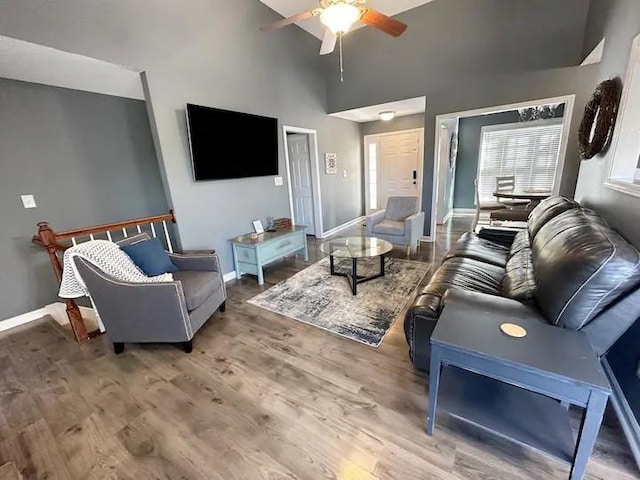 living area with a towering ceiling, ceiling fan, baseboards, and wood finished floors