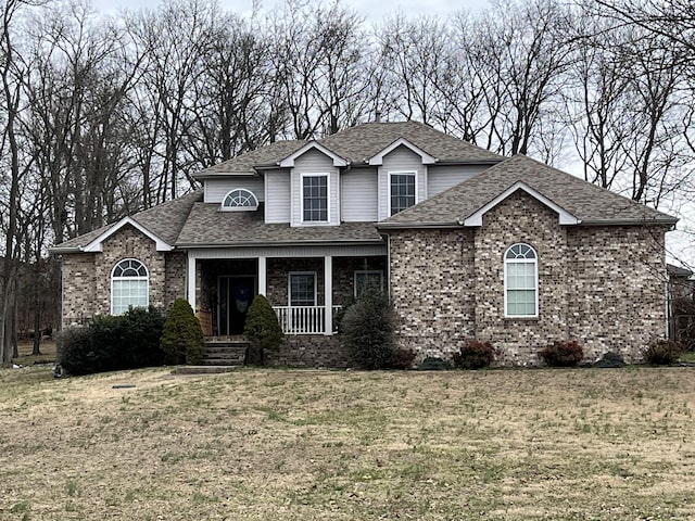 traditional-style home with brick siding, a porch, a front lawn, and roof with shingles