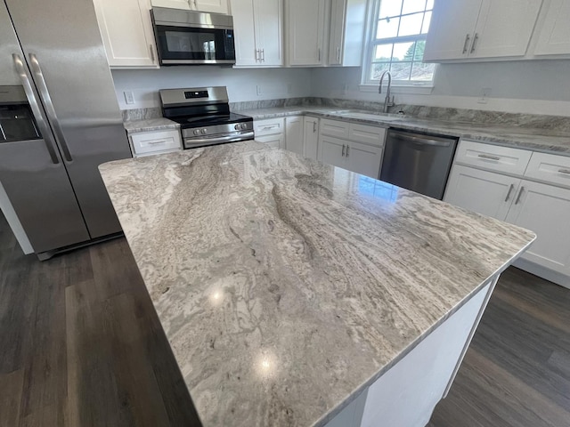 kitchen with dark wood finished floors, light stone counters, appliances with stainless steel finishes, white cabinets, and a sink