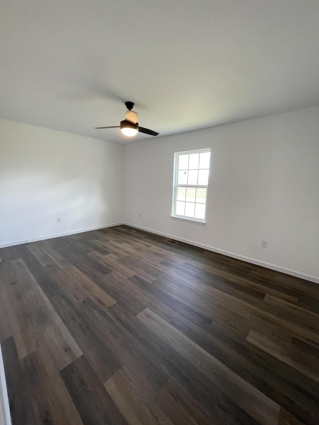 unfurnished room with a ceiling fan, baseboards, and dark wood-type flooring