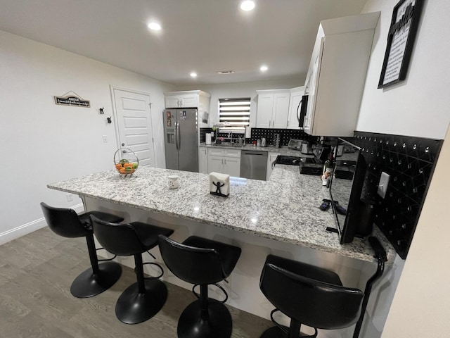 kitchen featuring white cabinets, appliances with stainless steel finishes, a breakfast bar area, a peninsula, and light stone countertops