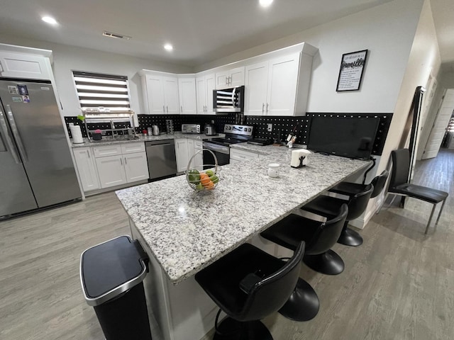 kitchen with stainless steel appliances, light wood-style floors, a breakfast bar area, and white cabinets