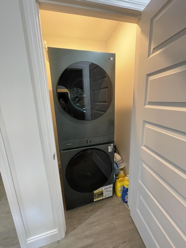 laundry area featuring wood finished floors, stacked washer and clothes dryer, and laundry area