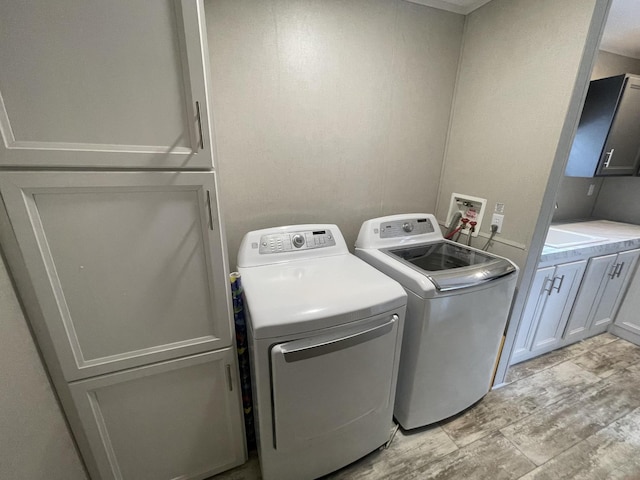 clothes washing area with cabinet space, separate washer and dryer, and light wood-style floors