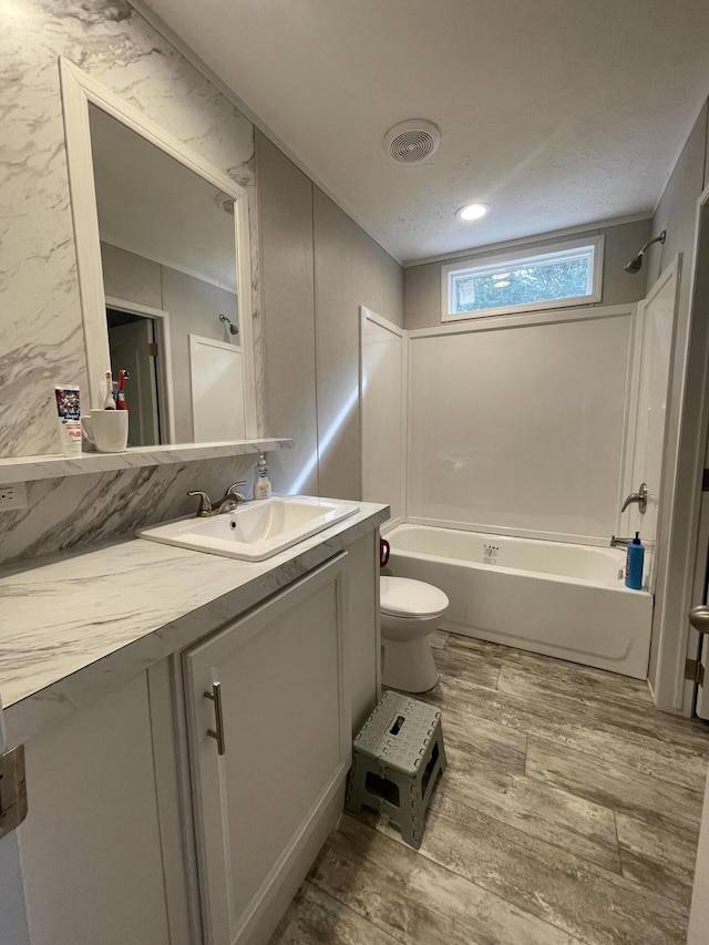 bathroom featuring visible vents, toilet, vanity, shower / tub combination, and wood finished floors