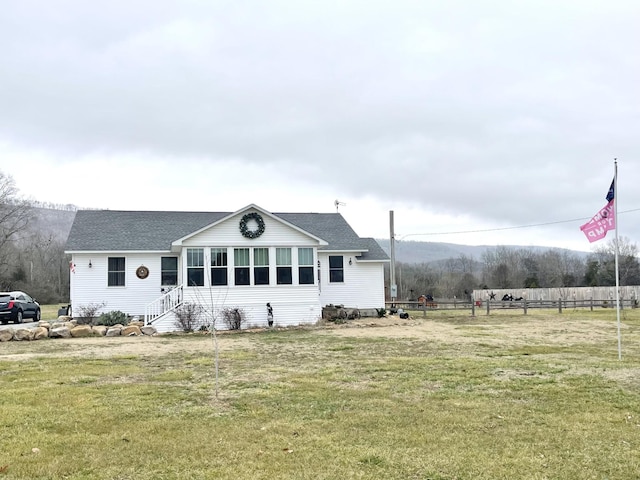 view of front of property with a shingled roof, fence, and a front yard