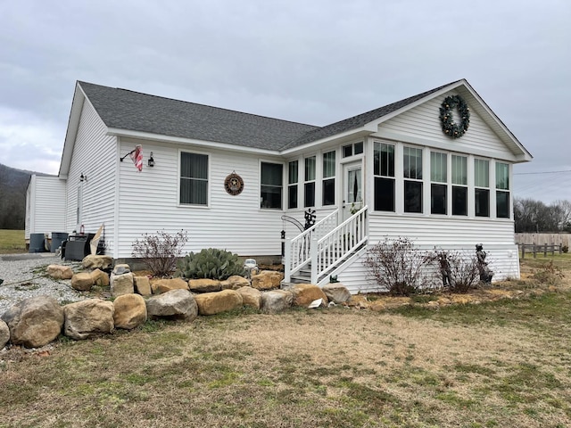 view of front of property featuring entry steps, a front lawn, and roof with shingles