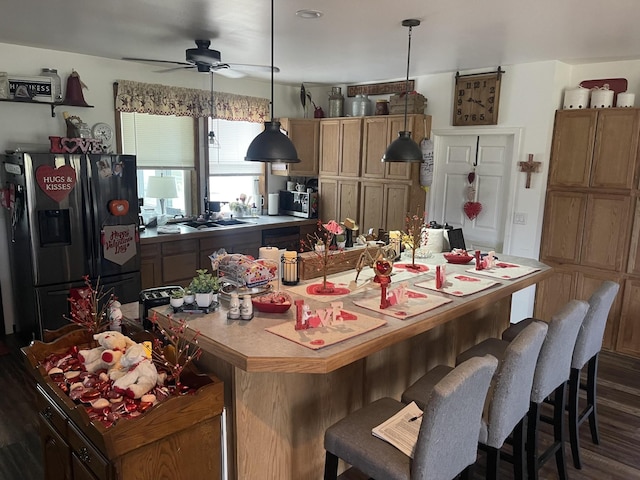 kitchen with dark wood-type flooring, a ceiling fan, hanging light fixtures, a center island, and stainless steel fridge