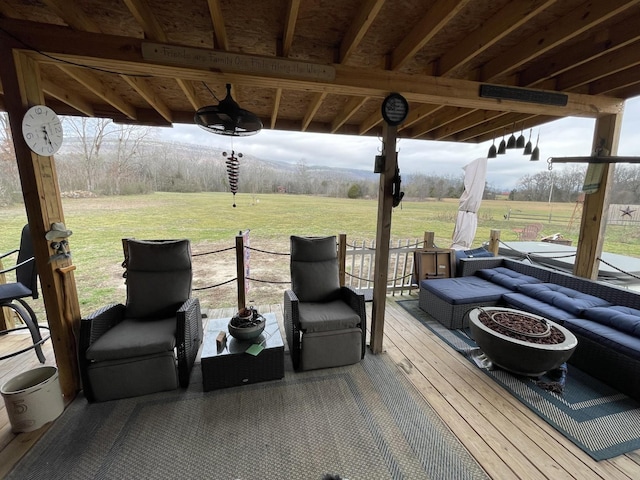 deck featuring a rural view, a ceiling fan, a lawn, and an outdoor living space with a fire pit