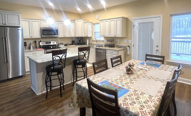 kitchen featuring a kitchen island, light stone counters, dark wood-style flooring, stainless steel appliances, and pendant lighting