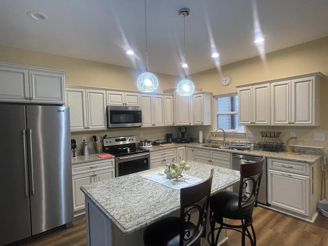 kitchen with appliances with stainless steel finishes, a center island, hanging light fixtures, light stone countertops, and a sink