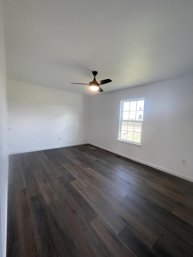 spare room featuring ceiling fan, dark wood finished floors, and baseboards