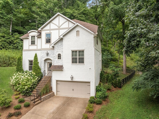 tudor house with roof with shingles, stucco siding, stairway, a garage, and driveway