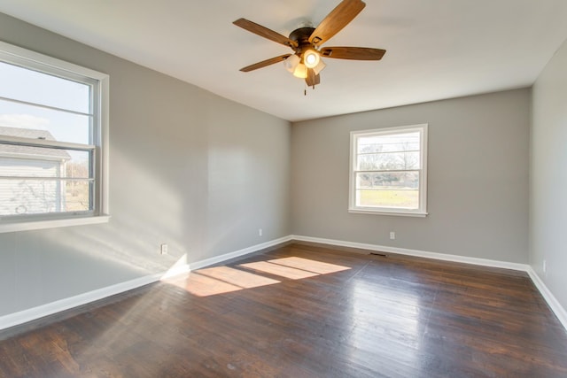 empty room with dark wood-type flooring, visible vents, ceiling fan, and baseboards