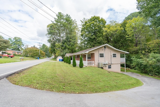 view of front facade featuring cooling unit, covered porch, a storage shed, driveway, and a front yard