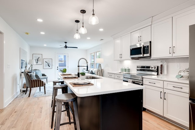 kitchen with an island with sink, a sink, stainless steel appliances, and light countertops