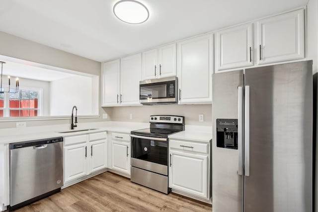 kitchen with white cabinets, light wood-style flooring, appliances with stainless steel finishes, light countertops, and a sink