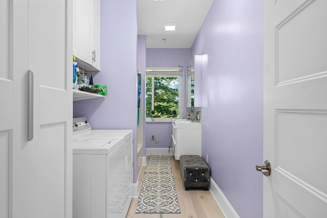 laundry area featuring light wood finished floors, washing machine and clothes dryer, cabinet space, a sink, and baseboards