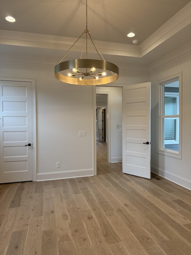 unfurnished room with light wood-style flooring, a notable chandelier, recessed lighting, baseboards, and a raised ceiling