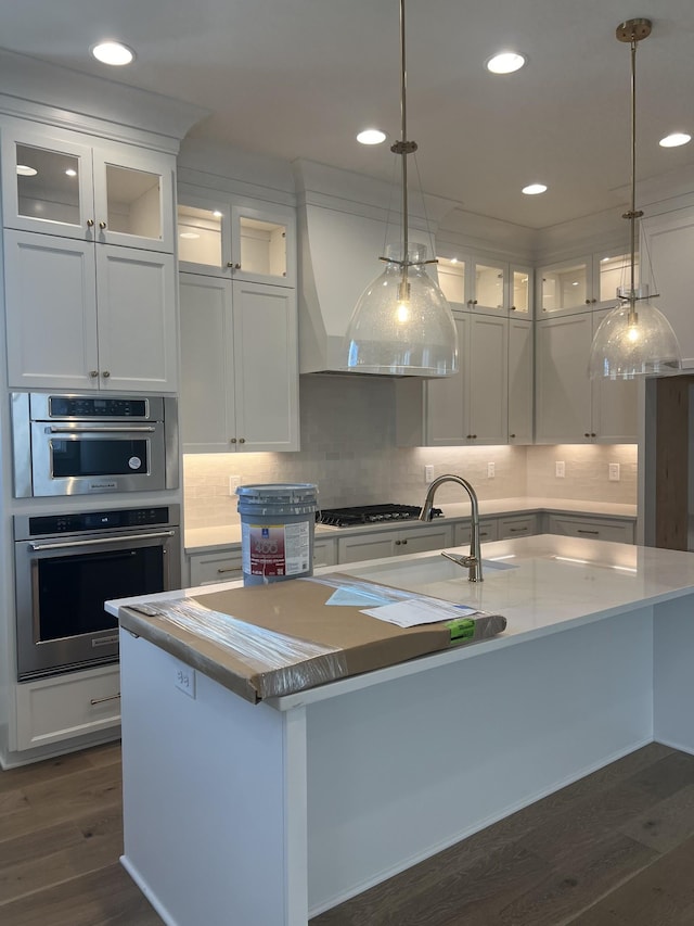 kitchen with stainless steel appliances, light countertops, dark wood-type flooring, a kitchen island with sink, and white cabinetry