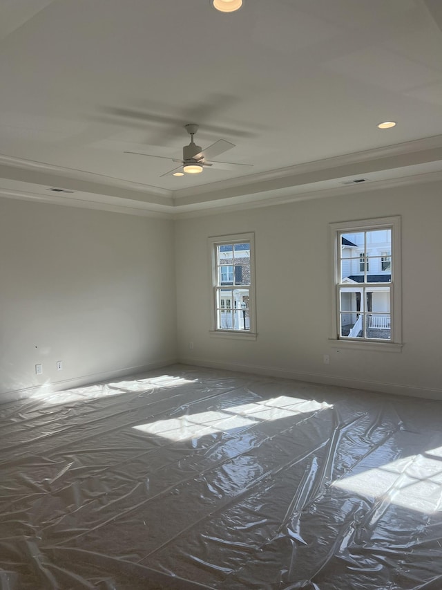 empty room with ceiling fan and a tray ceiling