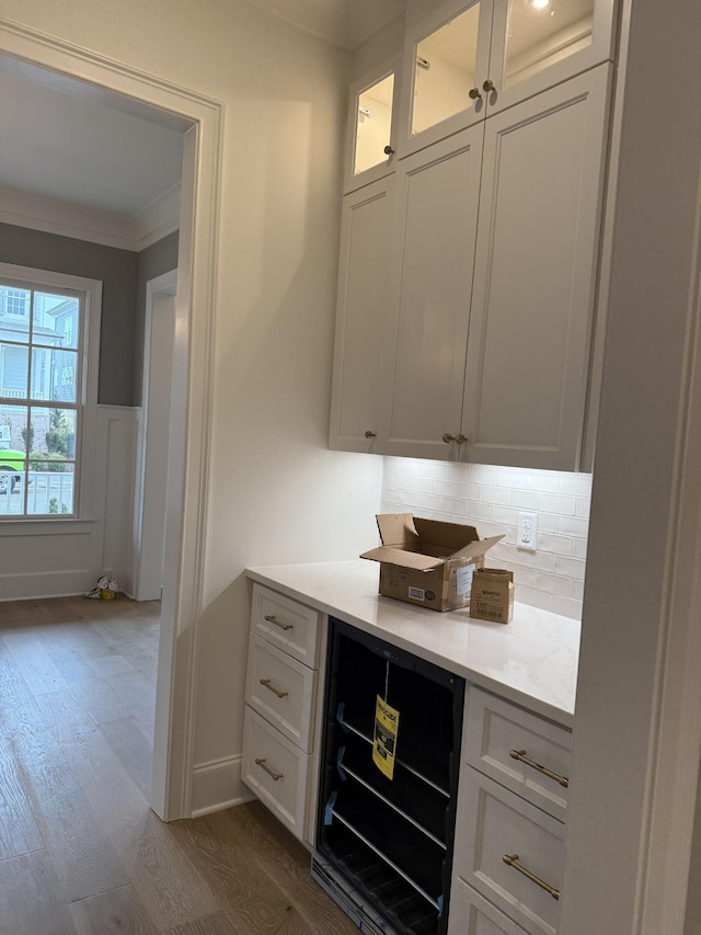 bar featuring wine cooler, dark wood-type flooring, wainscoting, decorative backsplash, and crown molding