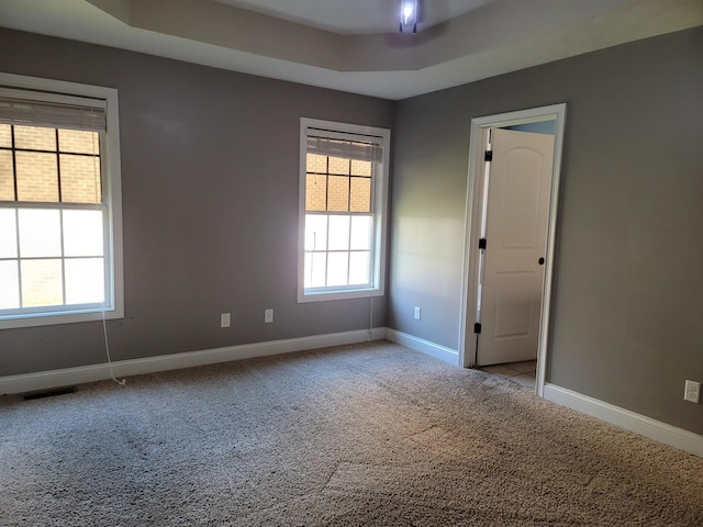 spare room featuring baseboards, a raised ceiling, visible vents, and light colored carpet